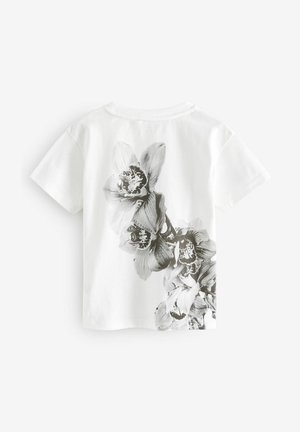 Tricou alb cu maneci scurte, prezentând un imprimeu floral alb-negru pe spate, înfățișând ilustrații detaliate de orhidee.
