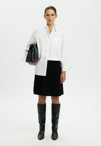 Balta pogu krekls ar kabatu, melns teksturēts līdz ceļiem veidots svārks un melni ādas zābaki līdz ceļiem. Tur rokassomiņu melnā krāsā.