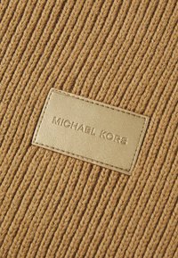 Tessuto a maglia marrone con texture a riga verticale, caratterizzato da un'etichetta in pelle dorata impressa con la scritta "MICHAEL KORS."