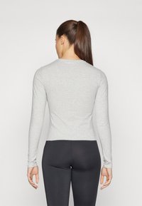 Garo rasas, gaiši pelēks krekls ar garām piedurknēm, izgatavots no mīksta, elastīga auduma. Tam ir apaļa kakla izgriezums un pieguļošs siluets. "Sweaty Betty" logo netālu no kakla izgriezuma.
