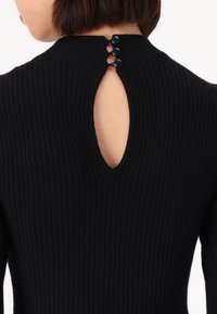 Haut en tricot noir à côtes avec une ouverture en forme de clé à l'arrière, maintenue par trois boutons noirs. Texture lisse, design ajusté.