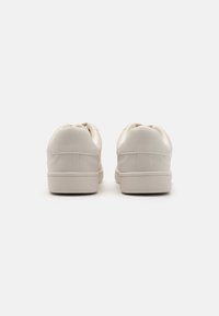 Białe sneakersy z gładką syntetyczną cholewką, zaokrąglonym tyłem, wyściełanym kołnierzem i teksturowaną gumową podeszwą. Widok z tyłu pokazuje minimalne detale.