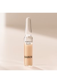 Ampoule en verre clair contenant un liquide beige clair. L'étiquette indique "PERFECT GLOW" en noir, avec le nom de la marque "BABOR" également en noir à la base.