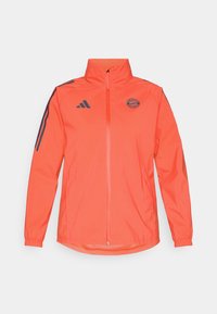 Feloranje, ritsjack met hoge kraag. Heeft donkerblauwe strepen op de schouders en een rond logo op de borst. Gladde textuur.