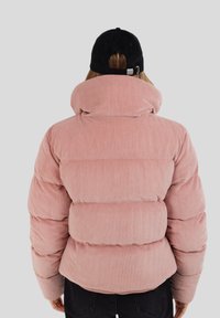 Różowa kurtka puchowa z włoskiej cordurowej tkaniny z wysokim kołnierzem, z żebrowaną fakturą i poziomym pikowaniem. Czarna czapka dopełnia stylizację.