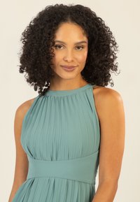 Plissiertes tealfarbenes Kleid mit Halfter-Ausschnitt und breitem Bund, das eine fließende Silhouette und eine weiche Textur bietet.