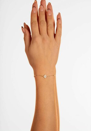 Guldkedja armband med en central stjärnformad berlock med en texturerad design, bärs på en hand med en naturlig nagelfinish.