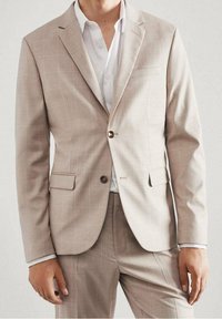 Beige colbert met ruitpatroon, enkele knoop, ingesneden revers en twee voorzakken, gecombineerd met een wit overhemd.