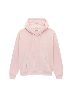 Sweat à capuche rose clair zippé avec poches avant, cordons de serrage et petit texte blanc imprimé sur le côté supérieur gauche de la poitrine.