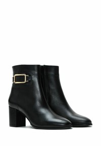 Bottines noires en cuir avec un bout pointu, un talon bloc, une fermeture éclair sur le côté et un accent en boucle dorée sur la sangle. Texture lisse.
