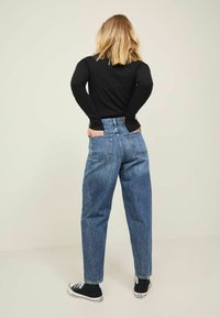 High-waisted blue denim jeans with a relaxed fit, featuring back pockets and frayed hem. Paired with black canvas sneakers.