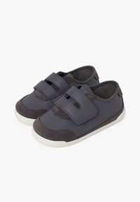 Sneaker grigie scure con cinturini in velcro, accenti in pelle scamosciata, parte superiore in pelle liscia e suola in gomma bianca. Design a punta rotonda per il comfort.