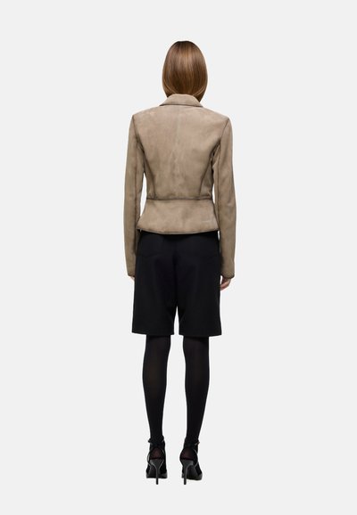 Beige suede jacket with lapel and tailored fit, paired with black tailored shorts, black tights, and high-heeled shoes.