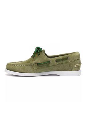Chaussure bateau en daim vert avec semelle blanche, lacets verts passés dans des œillets métalliques et détail décoratif de laçage latéral.