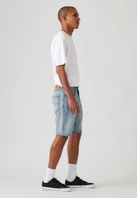 Tricou alb cu mânecă scurtă, pantaloni scurți din denim albastru, adidași negri și șosete albe. Croi lejer cu o siluetă dreaptă și margine desfăcută.