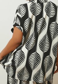 Camicia a maniche corte, bianca e nera, con motivo a foglie, tessuto testurizzato, colletto aperto e vestibilità ampia, mostrata dal retro.