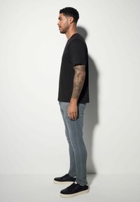 Tricou negru cu mânecă scurtă, blugi slăbiti gri deschis și adidași negri cu talpă albă, ilustrați dintr-o vedere laterală.