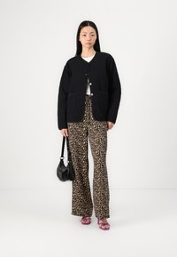 Black quilted jacket with buttons, two pockets; paired with leopard print wide-leg pants and purple heeled sandals. Black handbag held.