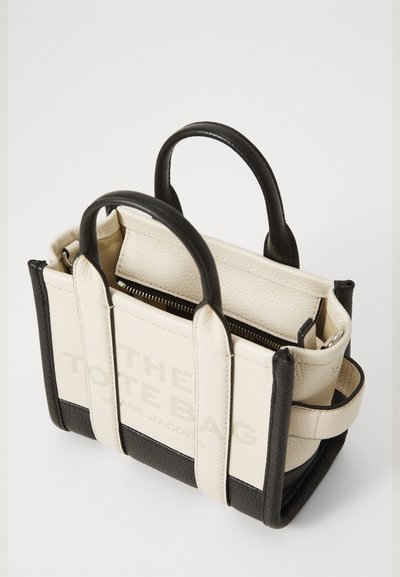 Compact tote bag made of smooth black and textured cream leather. Features dual top handles and a zip closure. Printed logo on the front.