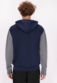 Felpa con cappuccio in navy e grigio dall'effetto liscio, dotata di cordino per regolare il cappuccio e maniche a contrasto. Presenta polsini e orlo a coste per una vestibilità aderente.