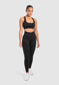 Schwarzer Sport-BH und hochgeschnittene Leggings aus dehnbarem Material mit figurbetontem Design. Kombiniert mit weißen Turnschuhen.