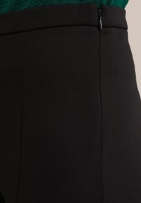 Melnas piegriezuma bikses ar gludu, teksturētu audumu. Iezīmējas ar sānu rāvējamo apģērbu un tīru šuvju detaļām.