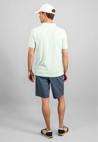 Ljusgrön pikétröja med korta ärmar, matchad med marinblå shorts och beige skor. Personen vänder ryggen mot kameran.