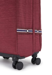 Red soft-shell suitcase with textured fabric, horizontal striped accents, and four black wheels for mobility.