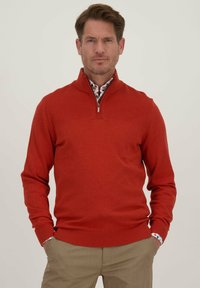 Rode gebreide pullover trui met een halve rits kraag, geribbelde manchetten en zoom. Draag het over een overhemd met een bloemenpatroon.