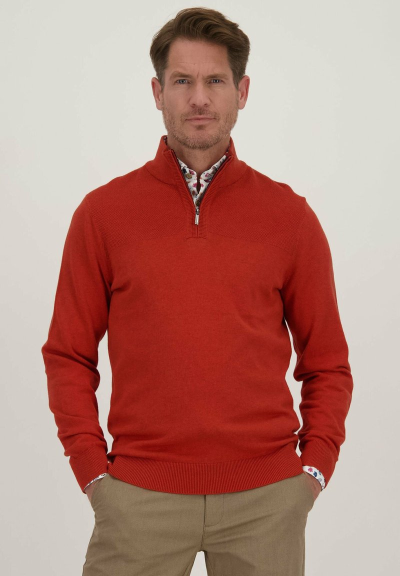 Rode gebreide pullover trui met een halve rits kraag, geribbelde manchetten en zoom. Draag het over een overhemd met een bloemenpatroon.