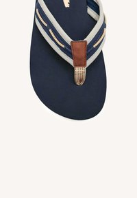 Chancla de marina con tira trenzada en gris y azul, acento de cuero marrón, plantilla texturada y diseño de suela circular.