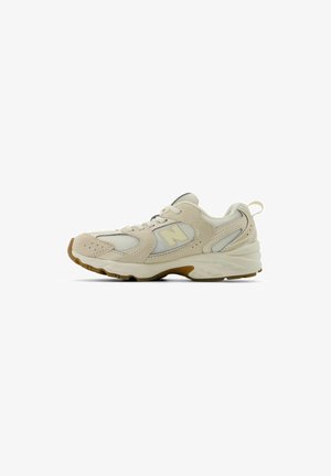 Beige Sport Schuh mit einem Obermaterial aus Netz und Wildleder, abgerundeter Zehenpartie, gepolsterter Sohle und einem markanten Logo an der Seite in einem hellgelben Akzent.