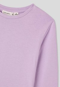 Fioletowa koszula z długim rękawem wykonana z miękkiej bawełny, z okrągłym dekoltem i prostymi detalami szycia. Widoczna metka z informacjami o marce i rozmiarze.