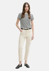 Camiseta de rayas blancas y negras, pantalones rectos cremosos con bolsillos; la modelo lleva un cinturón negro y mocasines negros sobre un fondo neutro.