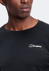Κοντινό πλάνο ενός ατόμου που φοράει μαύρο T-shirt Berghaus με στρογγυλή λαιμόκοψη και ορατό λογότυπο στο στήθος.