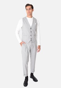 Completo tre pezzi grigio chiaro con gilet, revers classici, cinque bottoni e pantaloni plissettati; abbinato a mocassini neri.