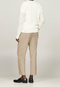 Kremowy sweter w warkocze z żeberkowym wykończeniem, w zestawieniu z jasnobeżowymi spodniami typu tapered i czarnymi skórzanymi mokasynami. Widok z tyłu.