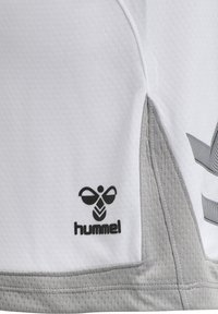 Vit sporttröja med strukturerad tyg, grå accentfärger och en svart logotyp med ett bi-design och ordet "hummel" längst ner till vänster.