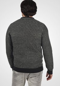 Suéter de patrón en blanco y negro con cuello redondo, puños y dobladillo acanalados, que muestra un diseño de punto texturizado en diagonal.