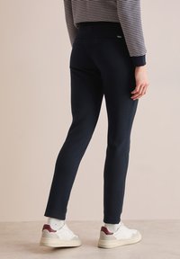 Navyblauwe fitted broek van een gestructureerde stof, met een middelhoge taille, achterzakken en gecombineerd met witte sneakers.