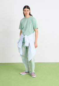 Svetlozelené bavlnené tričko s malým logom, svetlomodrá košeľa previazaná okolo pásu, vyblednuté modré džínsy a červeno-škótske slip-on topánky.