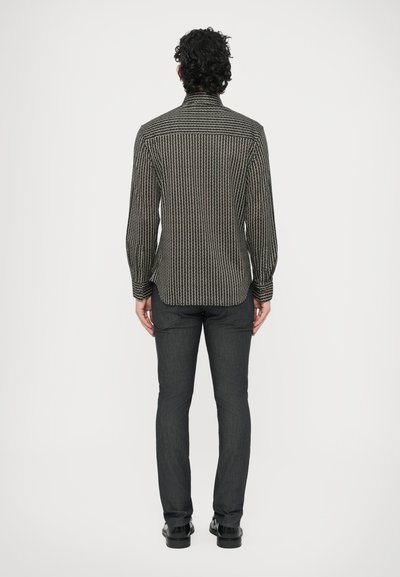 Juodu ir baltu raštuotas ilgomis rankovėmis marškinėliai su tiesiu kirpimu, dėvimi su tamsiai pilkais džinsais ir juodais batais, matomi iš nugaros.