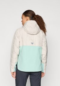 Lahka jakna z puhaso zasnovo v bež in mint zeleni barvi. Vključuje kapuco, pletene manšete in oznako na hrbtni strani.