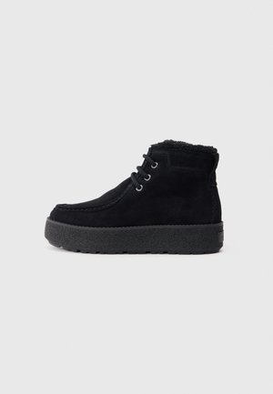 Bottines en suède noir avec une semelle en caoutchouc texturée. Les caractéristiques incluent des lacets ronds, une doublure en polaire et des détails de couture le long des bords.