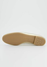 Světlehnědá plochá bota s hladkým, lesklým povrchem. Má zaoblenou špičku a minimalistický design. Podešev je světlehnědé barvy s embosovaným logem.