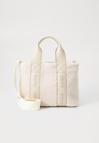 Beige faux shearling taske med cremefarvede læderhåndtag, der har en aftagelig skulderrem og præget logo-detalje på siderne.