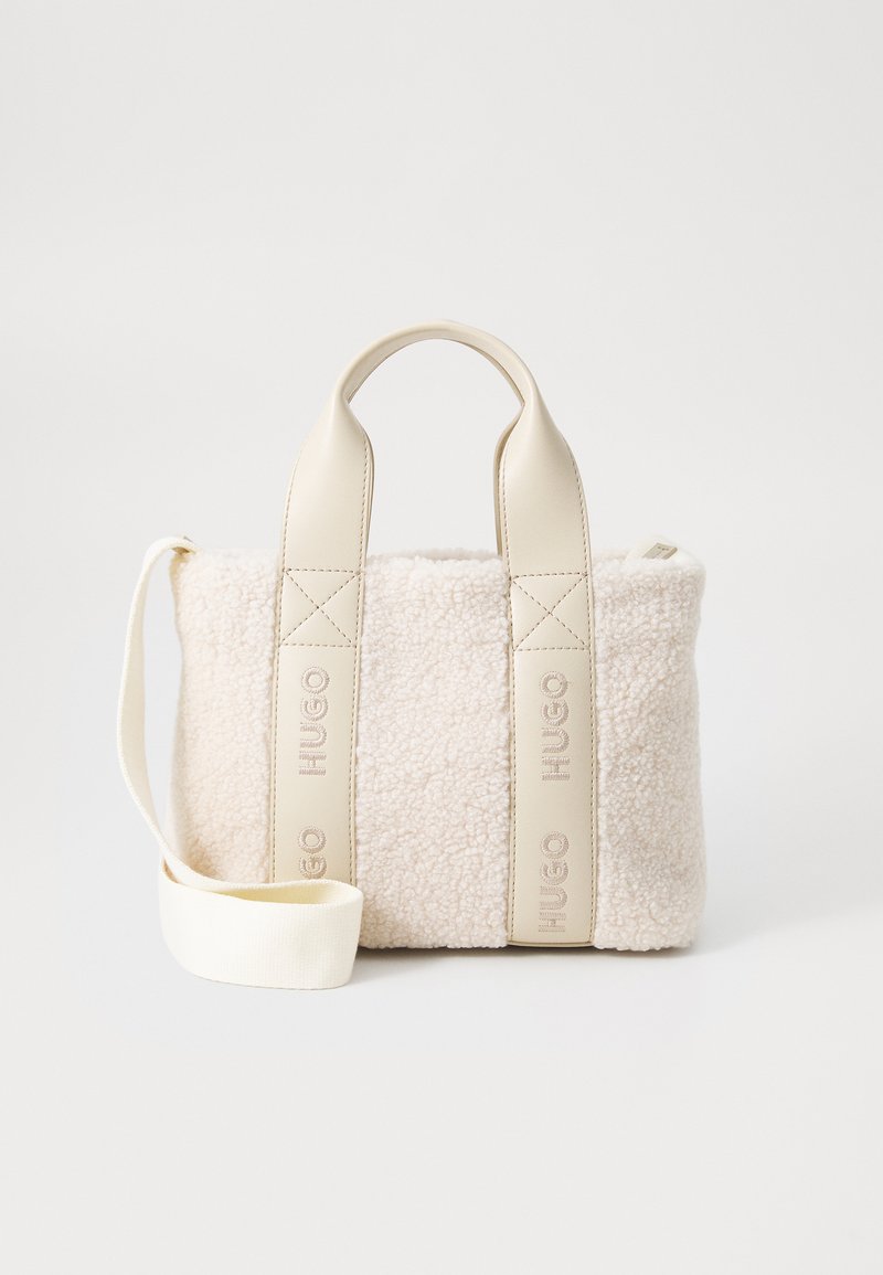 Beige faux shearling taske med cremefarvede læderhåndtag, der har en aftagelig skulderrem og præget logo-detalje på siderne.