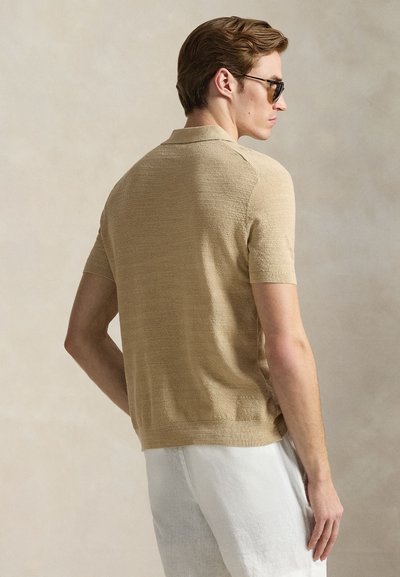 Ταμπά πλεκτό πουκάμισο πόλο με κοντά μανίκια και υφή στο ύφασμα, άνετη εφαρμογή και ριμπ γιακάς. Φορεμένο με ανοιχτόχρωμα σορτς.