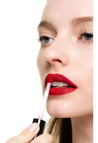 Se aplica un lápiz labial mate rojo con un aplicador en forma de pie de cierva. Los labios son carnosos y bien definidos, con una textura suave y uniforme.