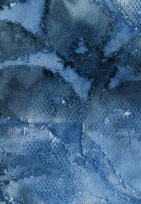 Denim fabric featuring various shades of blue with a textured surface, frayed edges, and a patterned weave.